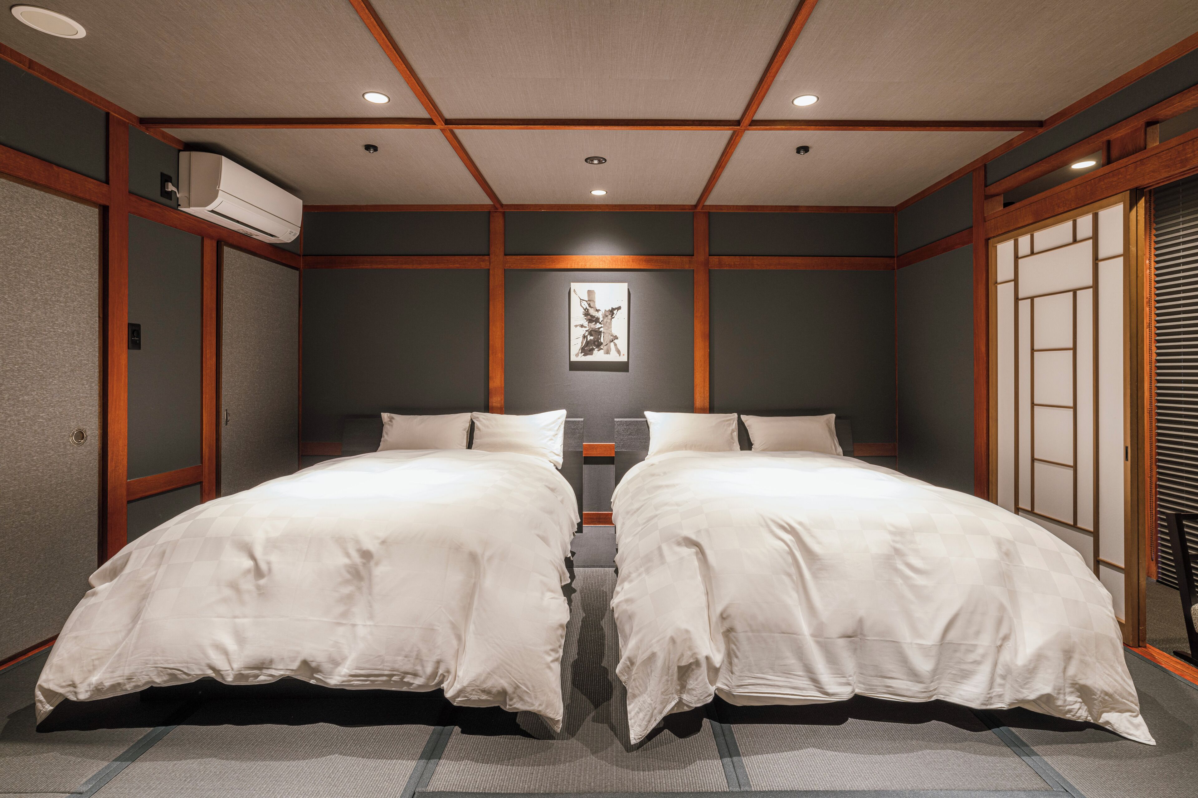 Ett hotellrum med två sängar, en takfläkt och en inramad tavla på väggen.