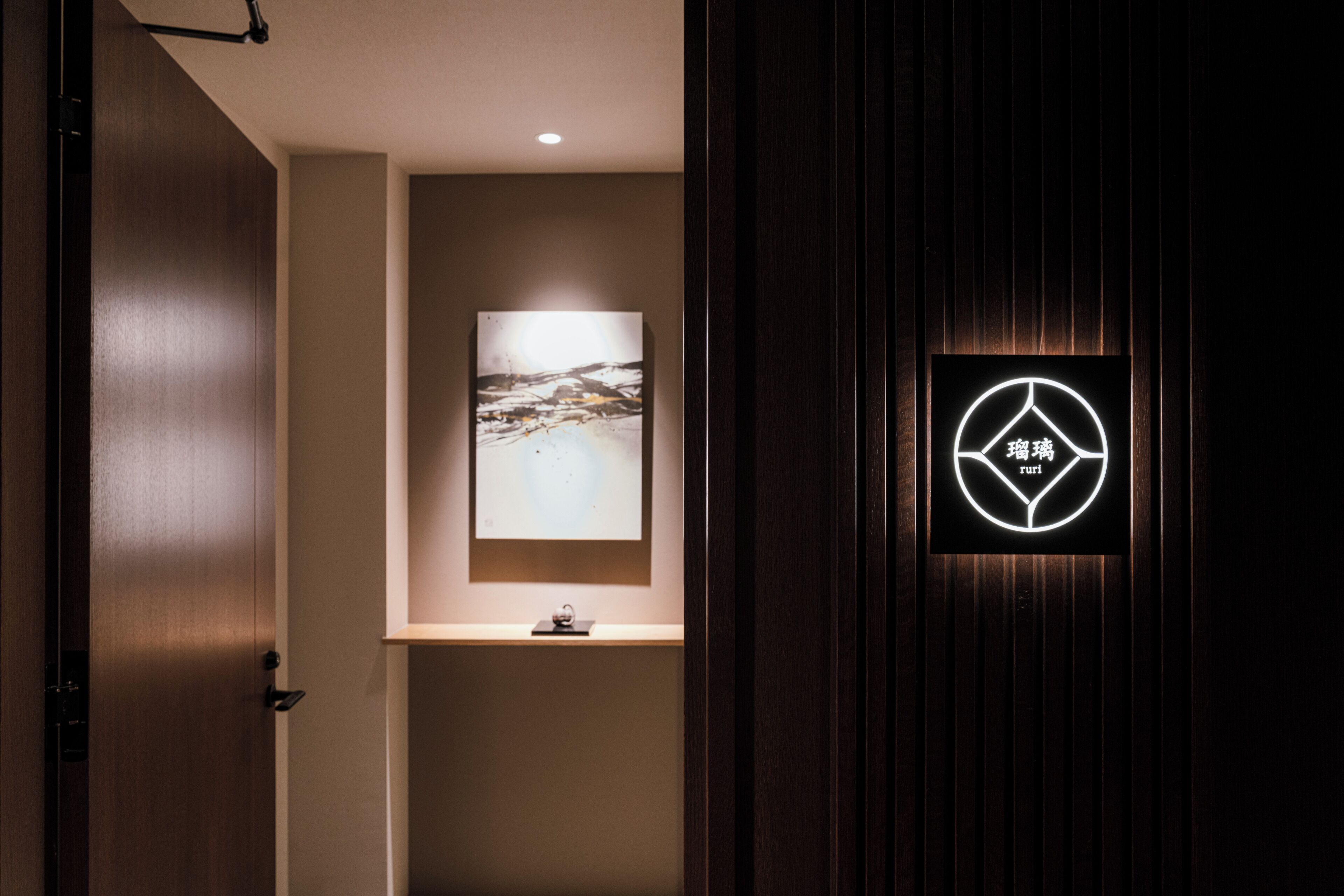 A hallway with a framed artwork on the wall, a small table, and a neon sign with text.