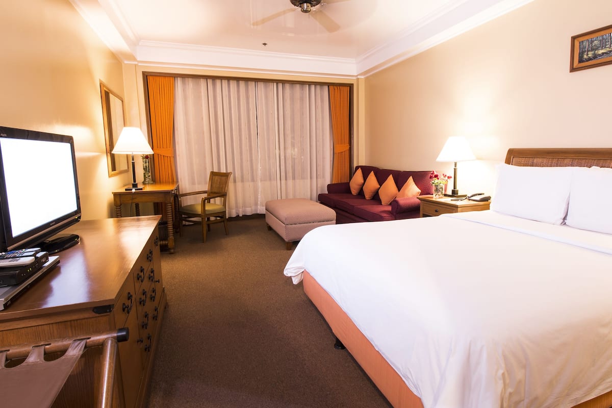 Quarto de hotel com uma cama, uma secretária com computador, uma cadeira, um sofá e uma televisão.