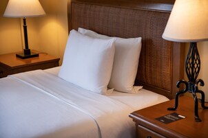 A neatly made bed with white linens and pillows, a wooden headboard, and two bedside lamps on wooden nightstands.