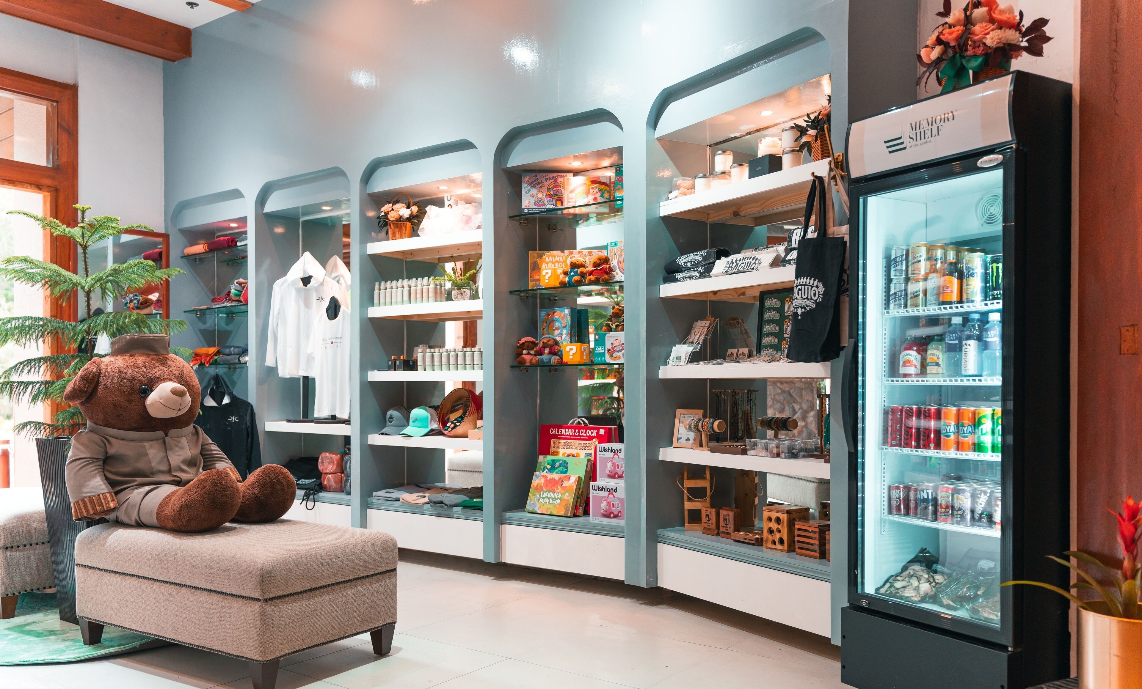 A cozy seating area with a plush chair and a large teddy bear, surrounded by shelves stocked with various items like toys, books, and snacks.