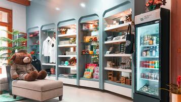 A cozy seating area with a plush chair and a large teddy bear, surrounded by shelves stocked with various items like toys, books, and snacks.
