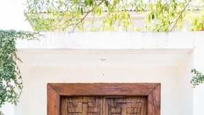A wooden double door with a brick pattern design, set in a white wall with a small overhang. - Allure Villas (Seminyak)