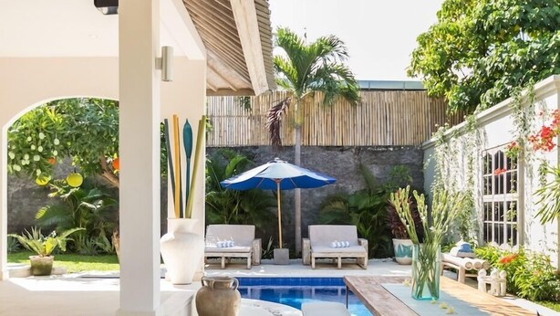 A covered outdoor area with a pool, wooden benches, lounge chairs, and potted plants. - Allure Villas (Seminyak)
