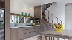 A modern kitchen with a marble countertop, wooden cabinets, and a yellow fruit basket on the dining table. - Allure Villas (Seminyak)