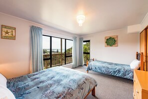 A bedroom with two beds, a chandelier, a view of the outdoors, and a wooden dresser. - Allure Lodge (Paihia)