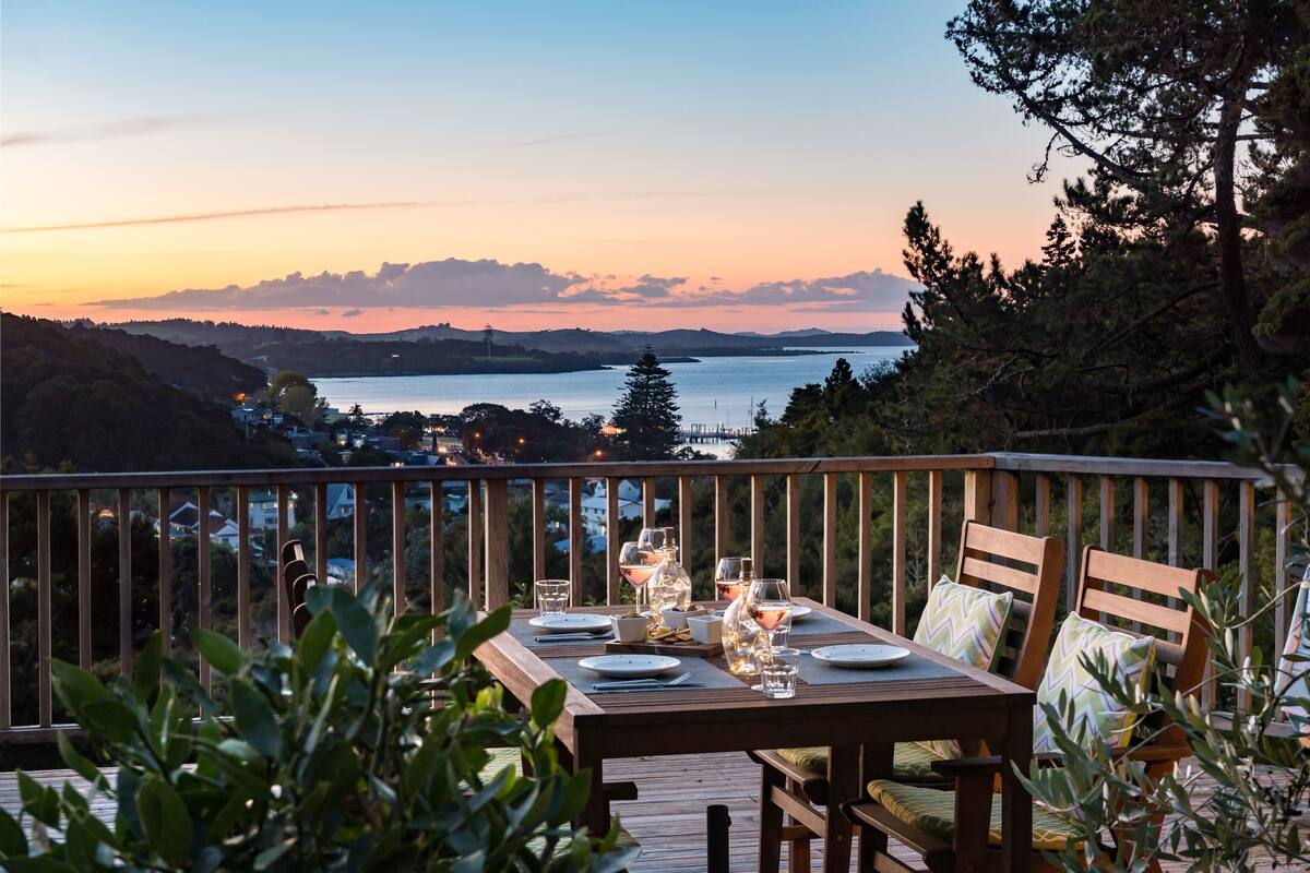 A wooden deck with a table set for dining, overlooking a lake and distant hills.