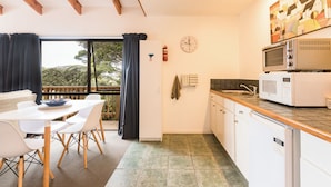 A modern kitchen with white cabinets, a microwave, and a sink. There is a dining area with a table and chairs. - Allure Lodge (Paihia)
