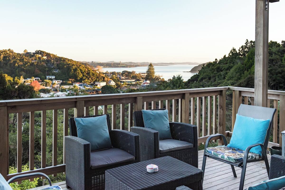A deck with wicker furniture and a view of a coastal town.