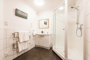 A modern bathroom with a glass-enclosed shower, a white sink, and a tiled floor. - Allure Lodge (Paihia)