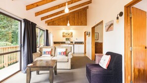 A cozy living room with a sofa, a coffee table, and a dining area with a kitchen in the background. - Allure Lodge (Paihia)