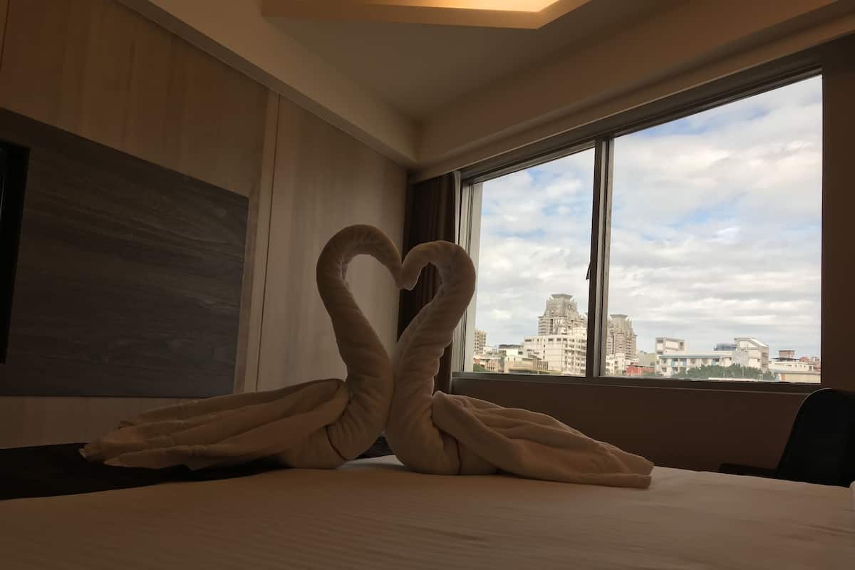 A hotel room with a bed, a large window, and a view of buildings.