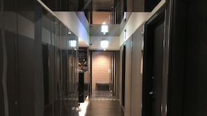 A modern hotel corridor with glass walls, a tiled floor, and a central light source.