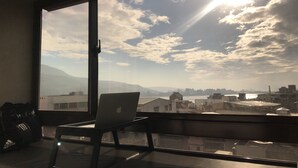 A room with a large window, a laptop on a desk, and a chair.