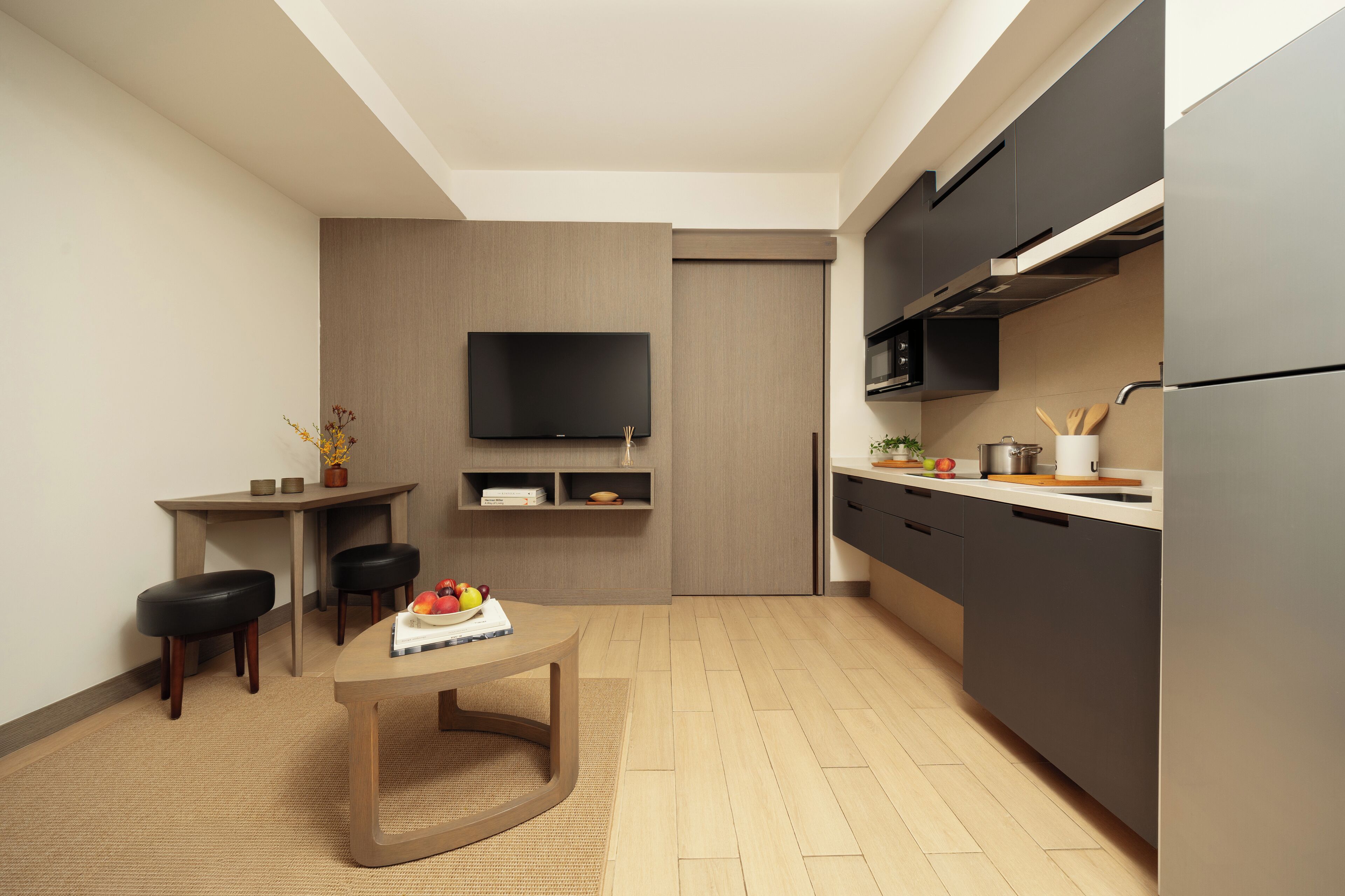 Una cocina moderna con un televisor de pantalla plana, armarios oscuros y una mesa de comedor de madera con fruteros.