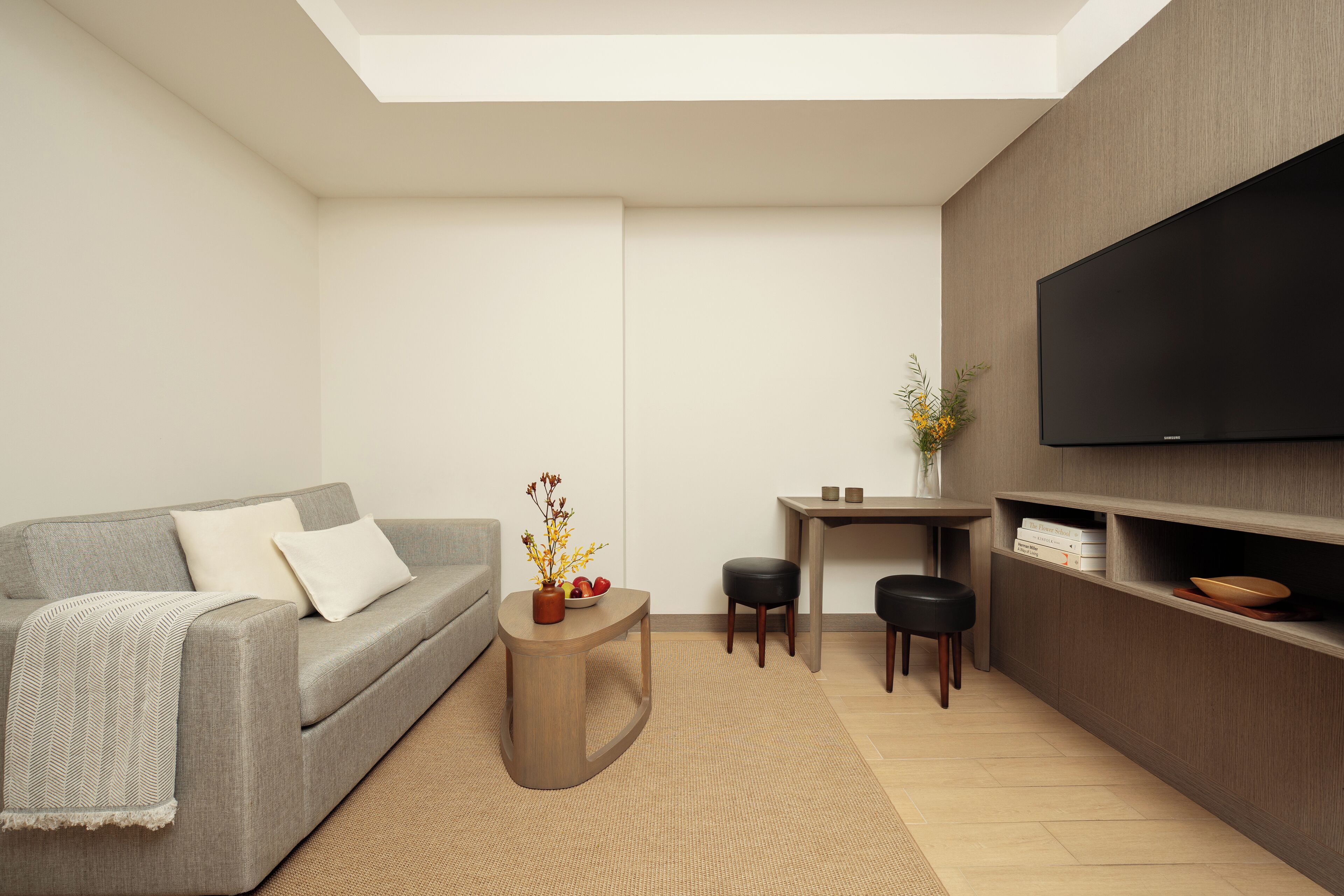 Ein modernes Wohnzimmer mit grauem Sofa, einem kleinen Holztisch, einem flachbildfernseher an der Wand und einem minimalistischen Design.