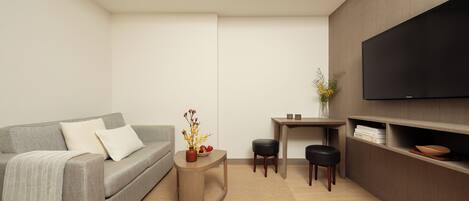 Ein modernes Wohnzimmer mit grauem Sofa, einem kleinen Holztisch, einem flachbildfernseher an der Wand und einem minimalistischen Design.