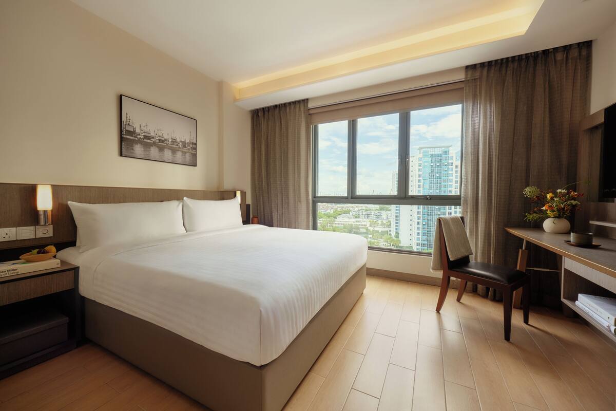 A hotel room with a large bed, a desk, a chair, a TV, and a window with a city view.