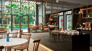 Un café moderno con un amplio ventanal de vidrio, muebles de madera y diversos productos de comida y bebida exhibidos en la barra.