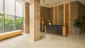 Una moderna zona de recepción con un mostrador de madera, ventanas amplias y una lámpara de pie alta y cilíndrica.