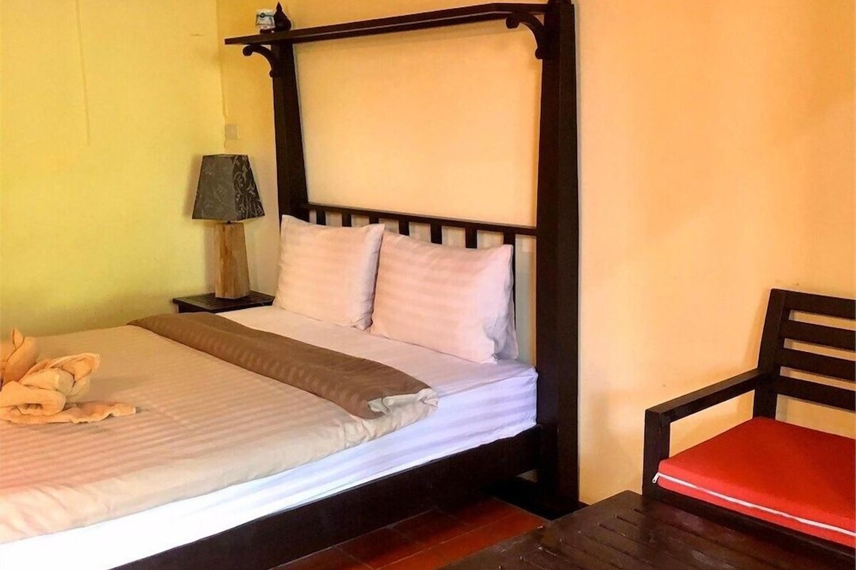 A bed with a wooden headboard, a bedside table, a lamp, and a chair with a red cushion.