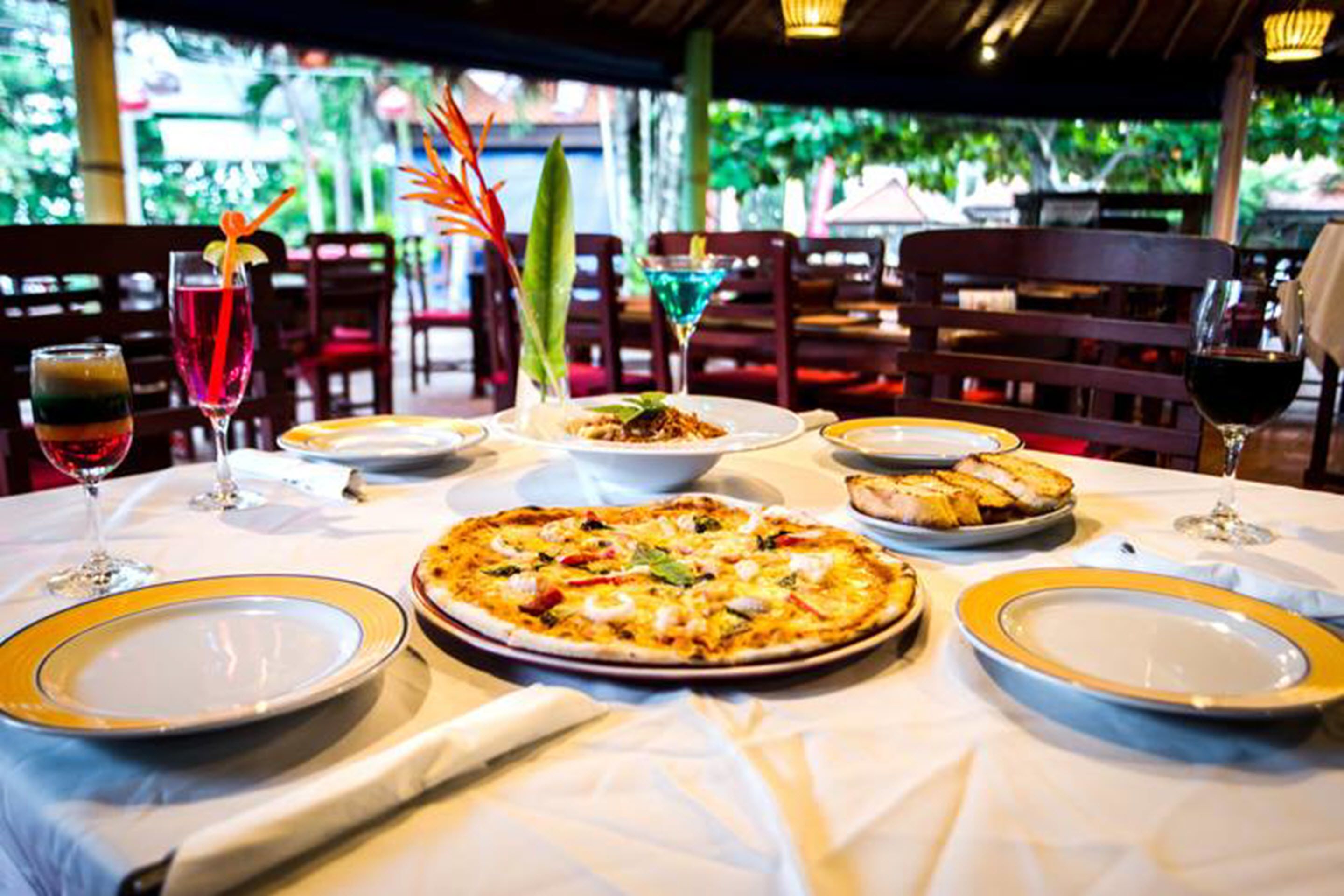 A restaurant table set with a pizza, plates, glasses, and a decorative centerpiece.
