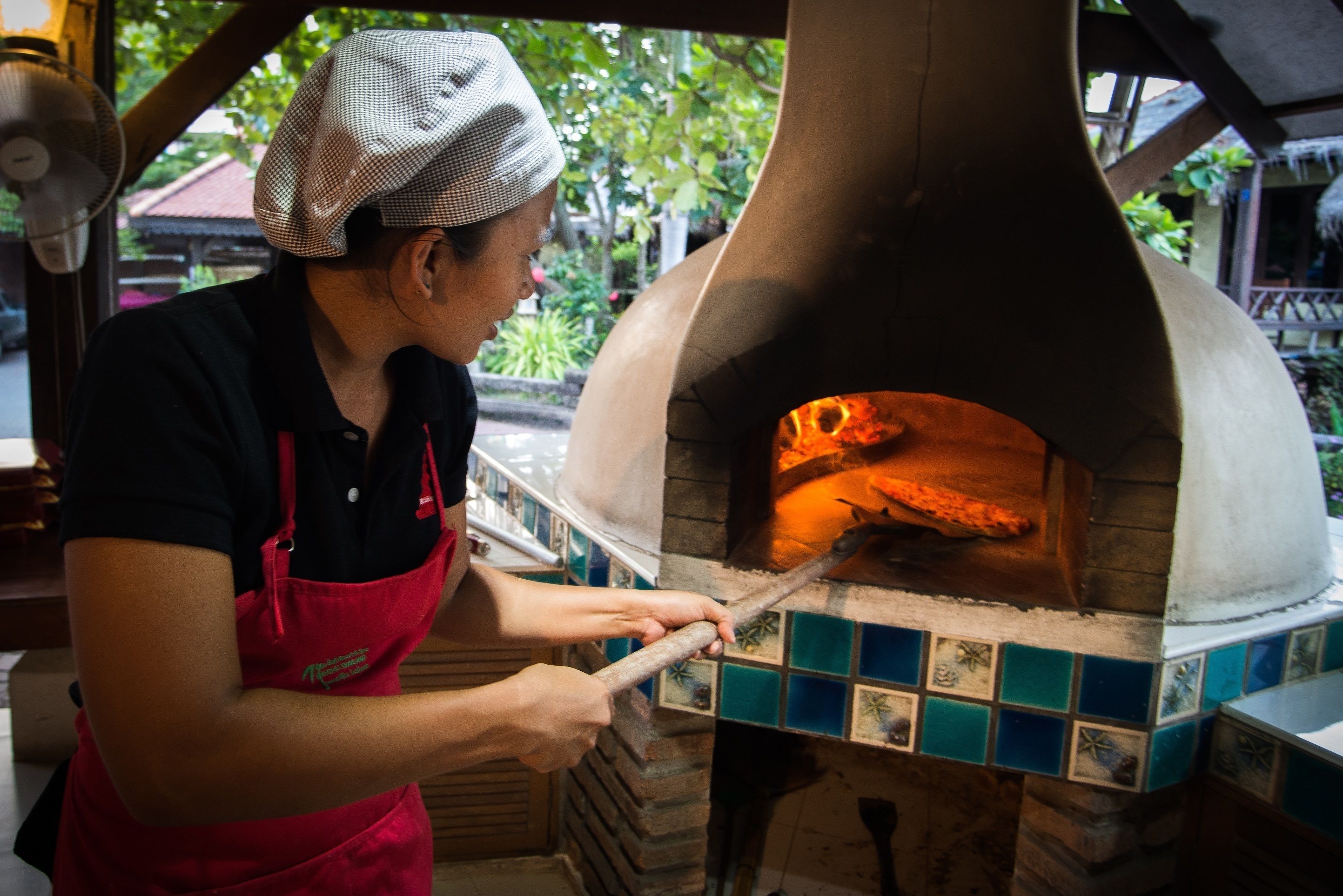 Una persona usando una herramienta de mango largo para controlar un horno de pizza.