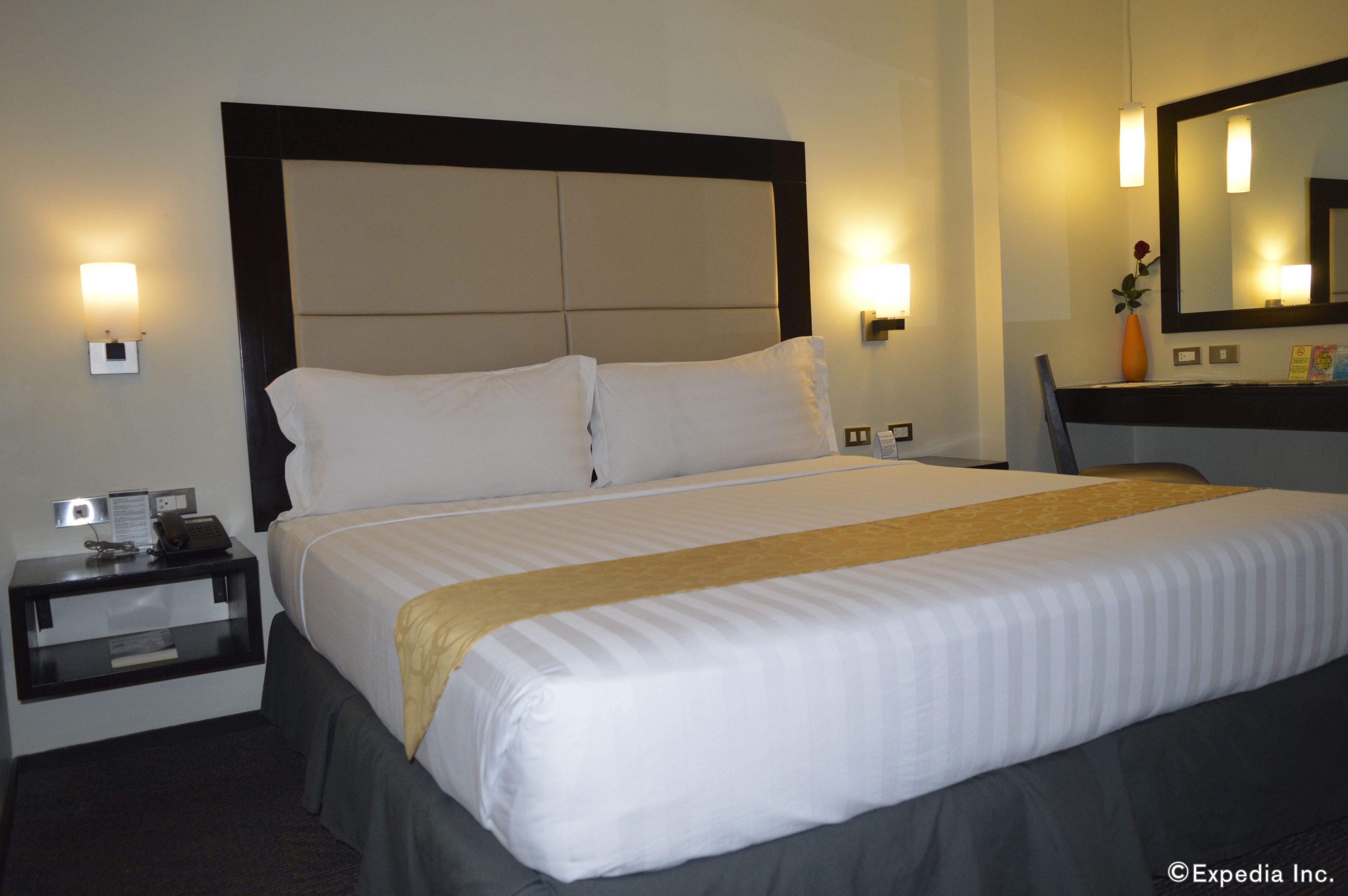 Una habitación de hotel con una cama grande, una mesita de noche, un escritorio y un espejo.