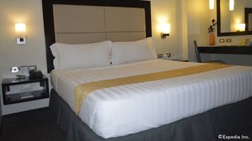 Una habitación de hotel con una cama grande, una mesita de noche, un escritorio y un espejo.
