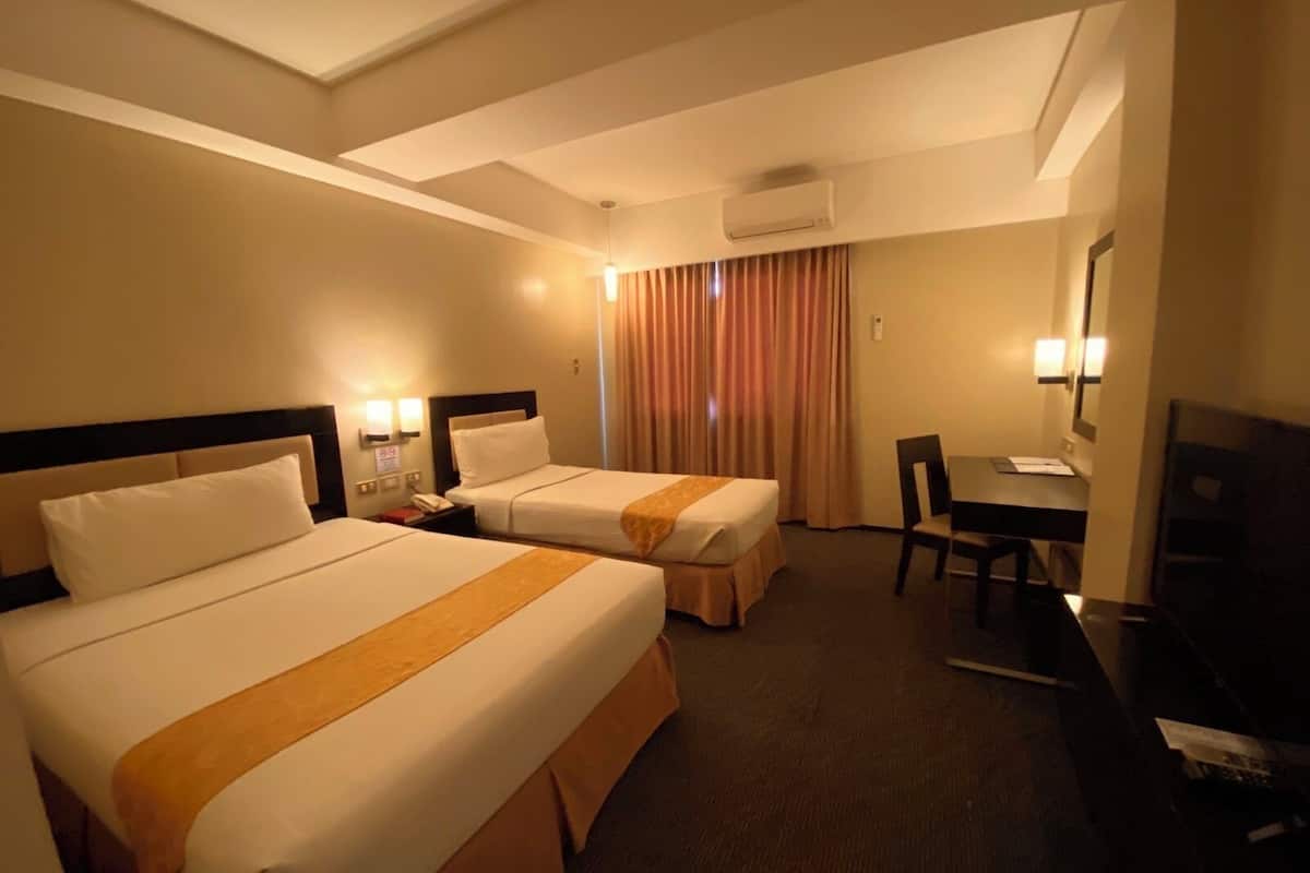 Une chambre d’hôtel avec deux lits, un bureau, une chaise, un appareil de climatisation et un téléviseur.
