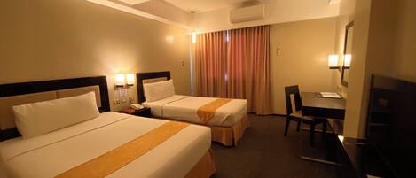A hotel room with two beds, a desk, a chair, an air conditioning unit, and a television.
