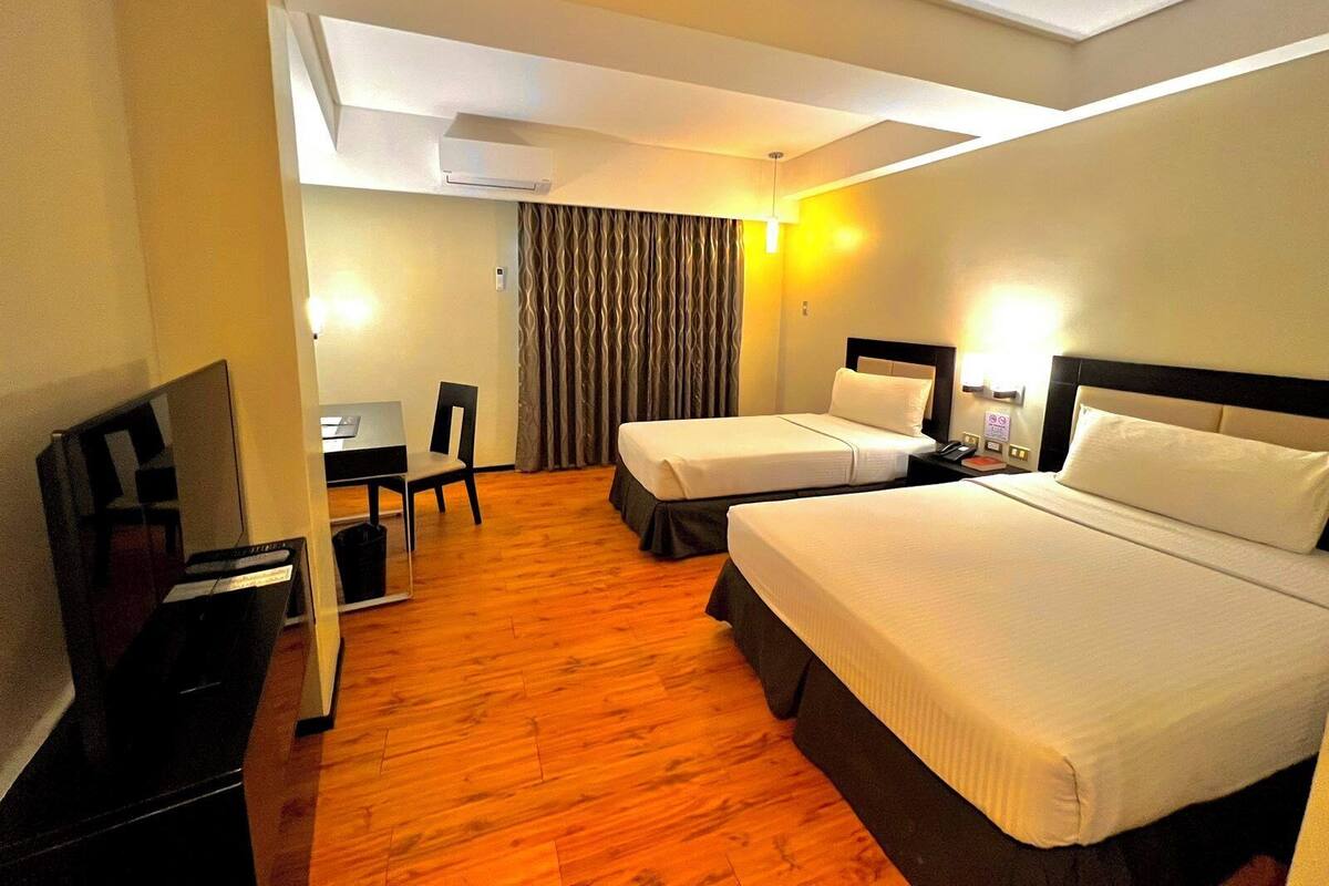 Une chambre d’hôtel avec deux lits, un bureau, une chaise, une télévision et un appareil de climatisation.