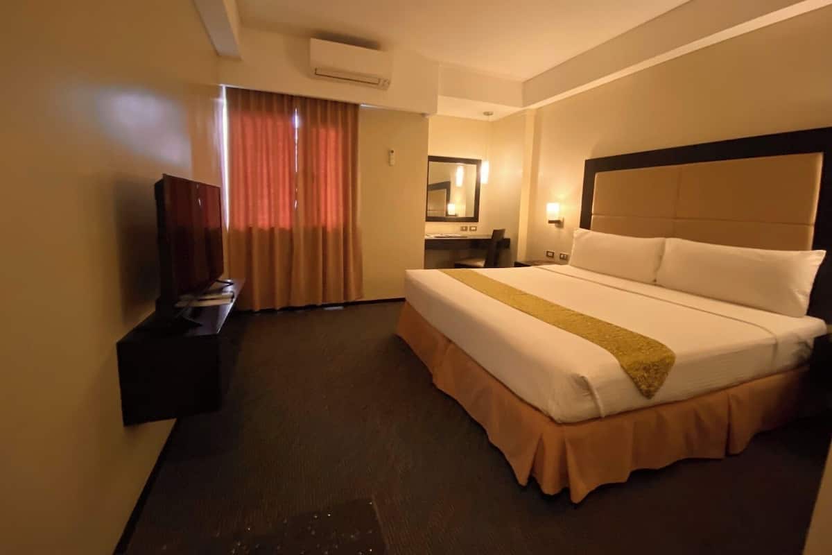 Une chambre d’hôtel avec un grand lit, un bureau, une chaise, une télévision et une fenêtre avec des rideaux.