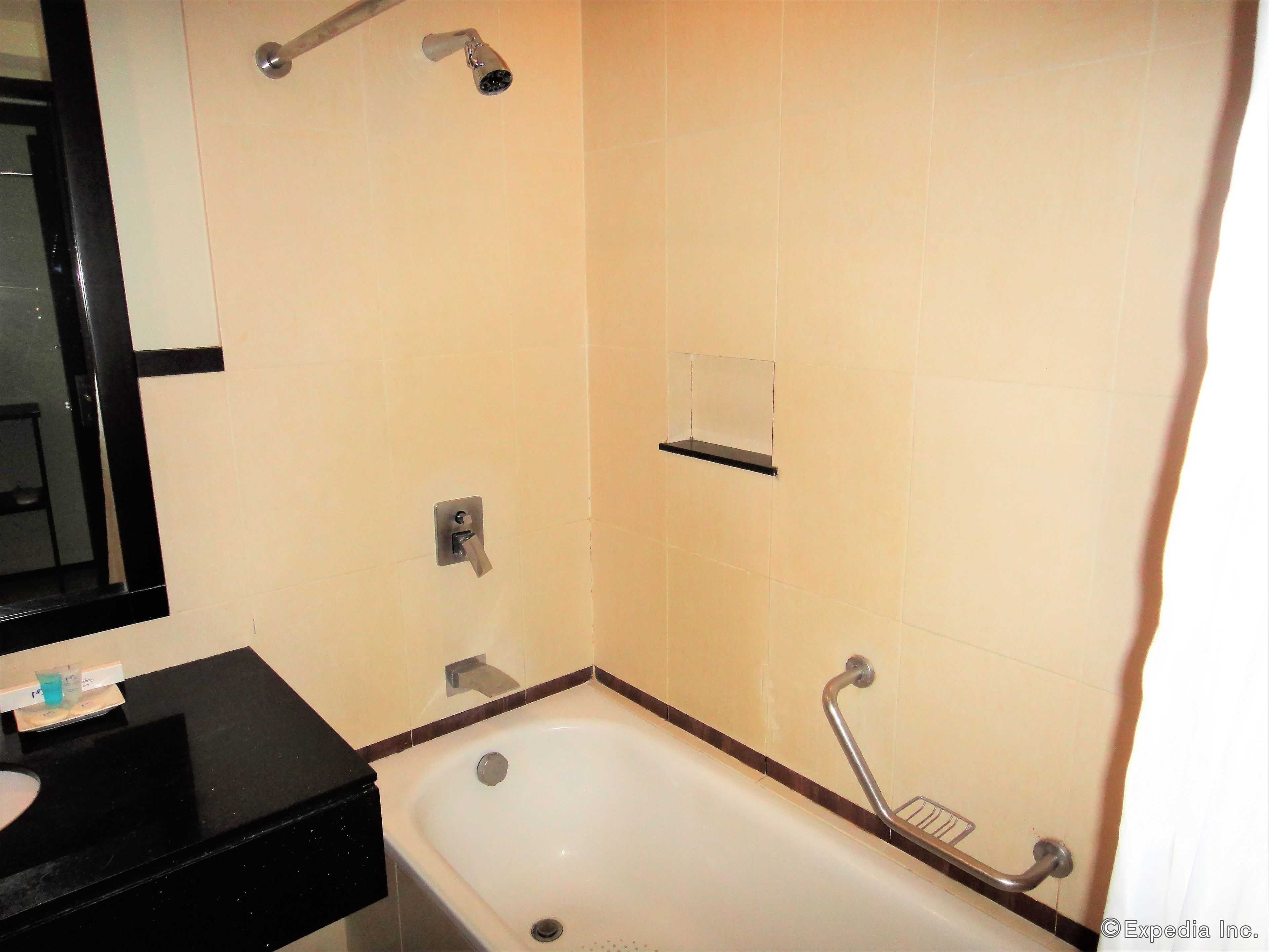 A bathroom with a bathtub, a shower head, a towel rack, and a soap dispenser.