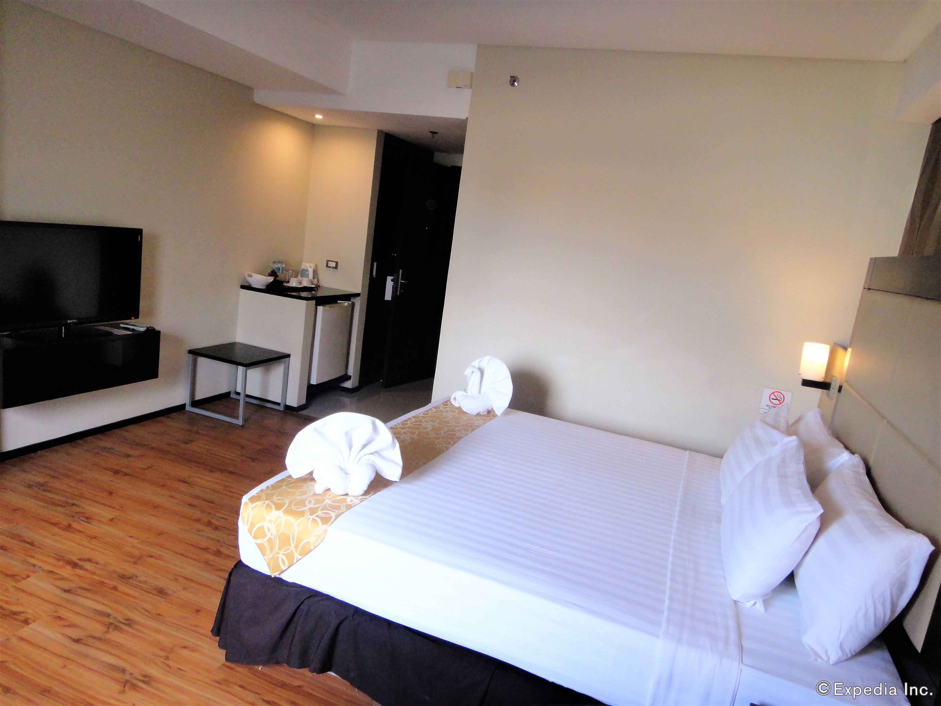 A hotel room with a bed, a TV, a desk, and a small kitchenette.