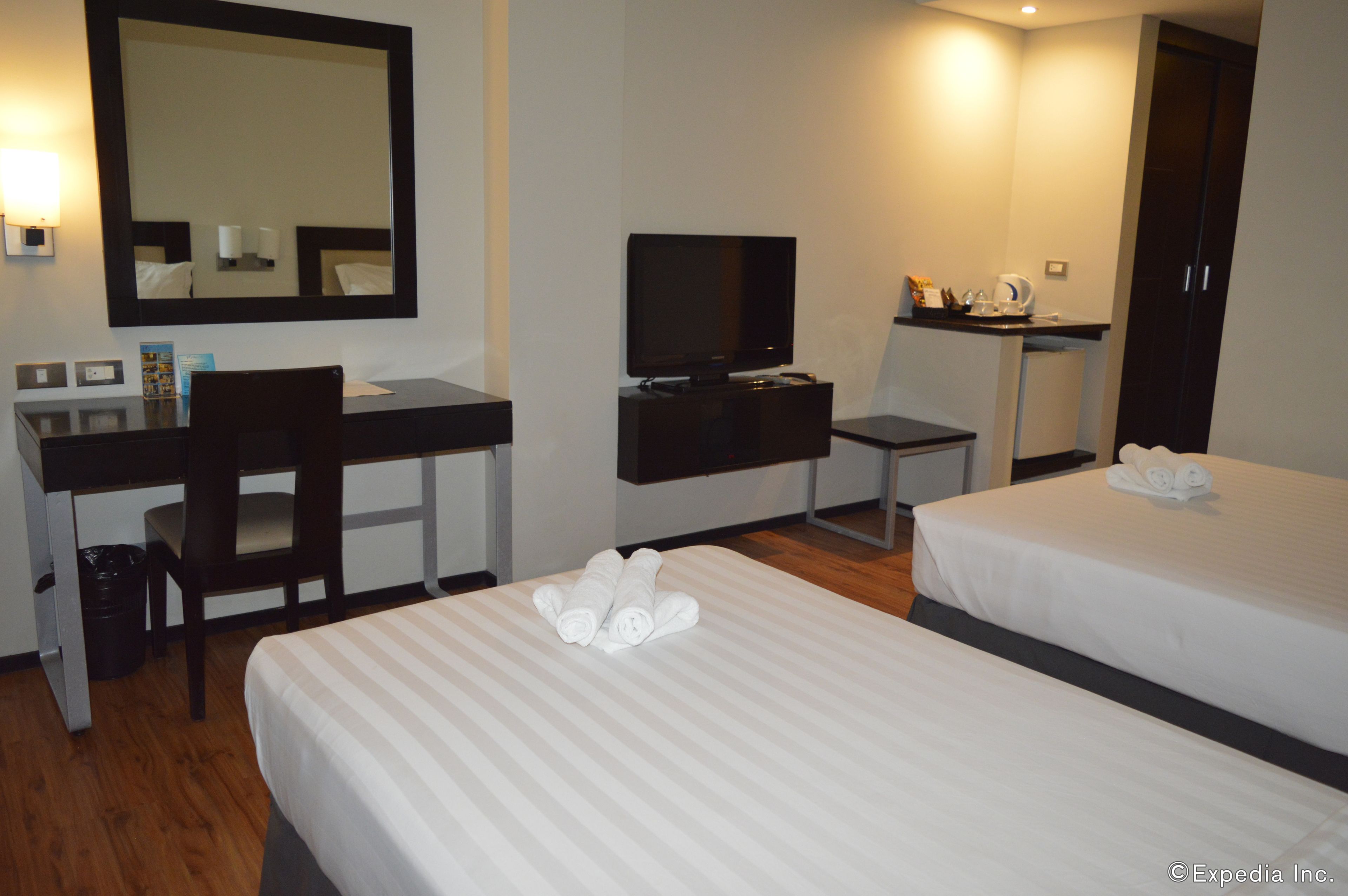 A hotel room with two beds, a desk, a television, and a mirror.