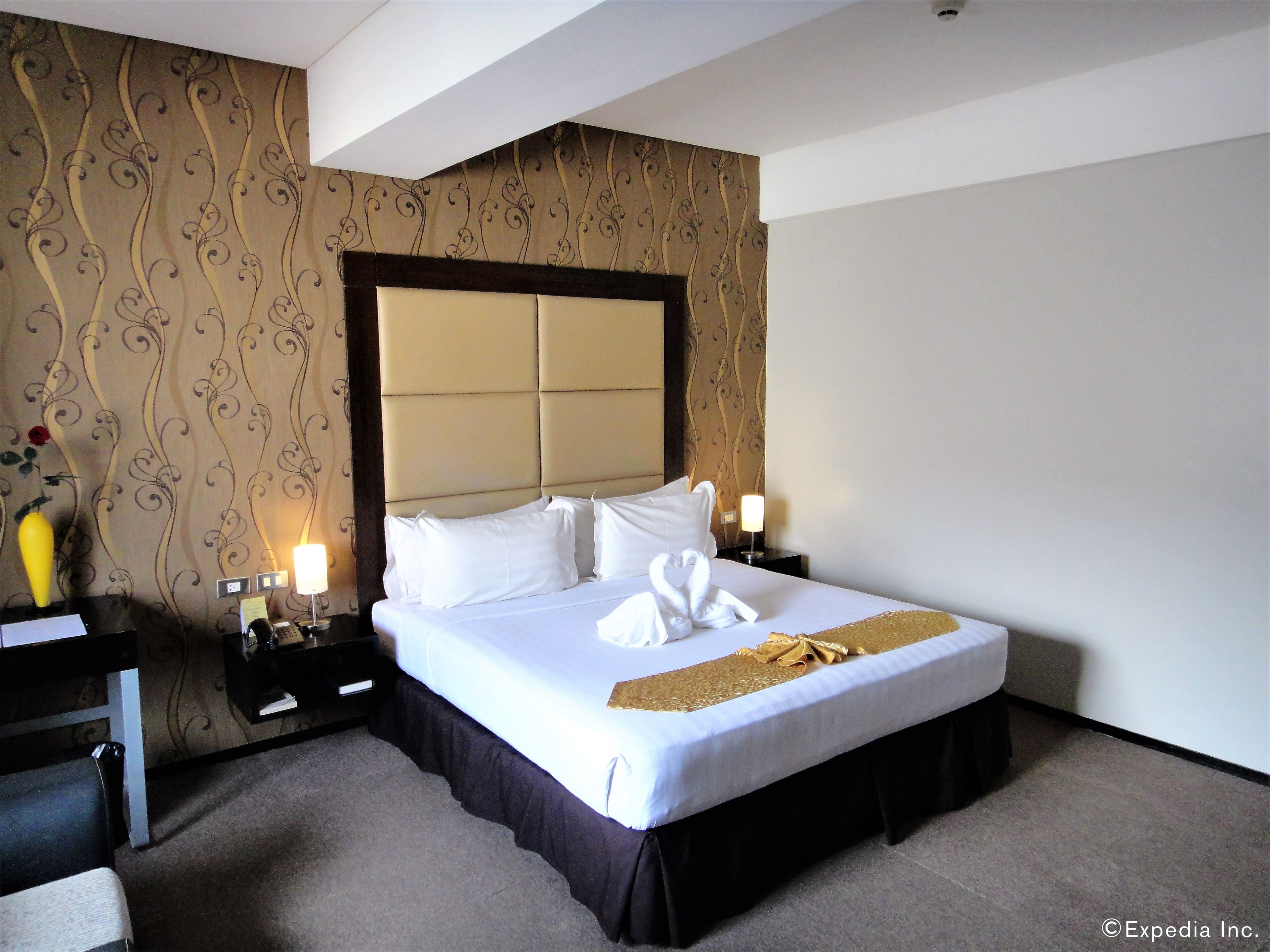 A hotel room with a large bed, a nightstand, a lamp, and a decorative vase.