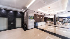Een moderne hotellobby met een receptiebalie, zithoek en een café.