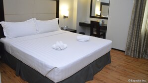 Hotelkamer met een groot bed, nachtkastje, bureau, stoel, spiegel en raam met gordijnen.