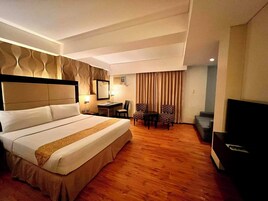 Habitación de hotel con una cama grande, un escritorio, dos sillas, un televisor y un sofá.