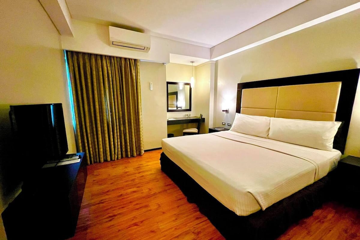 Une chambre d’hôtel avec un grand lit, un bureau avec une chaise, une télévision et un miroir.