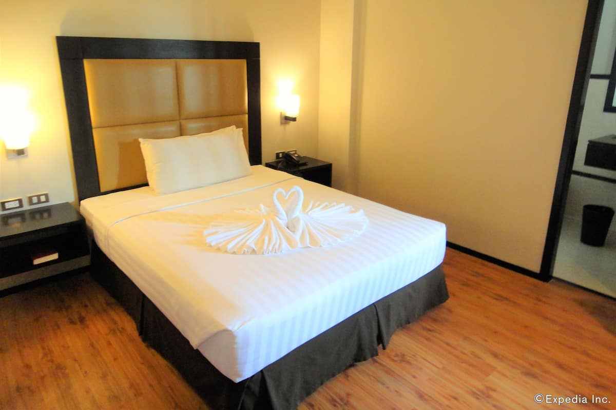 Une chambre d’hôtel avec un grand lit, une tête de lit, deux tables de chevet, une petite table et une lampe fixée au mur.