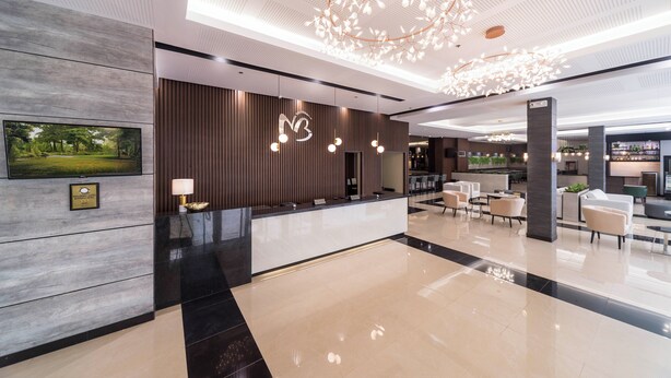 Een moderne hotellobby met een receptiebalie, zithoek en een grote kroonluchter.
