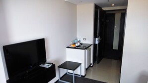 Een compacte hotelkamer met een flatscreen-televisie, een klein tafeltje met een waterkoker en fruit, en een kitchenette.