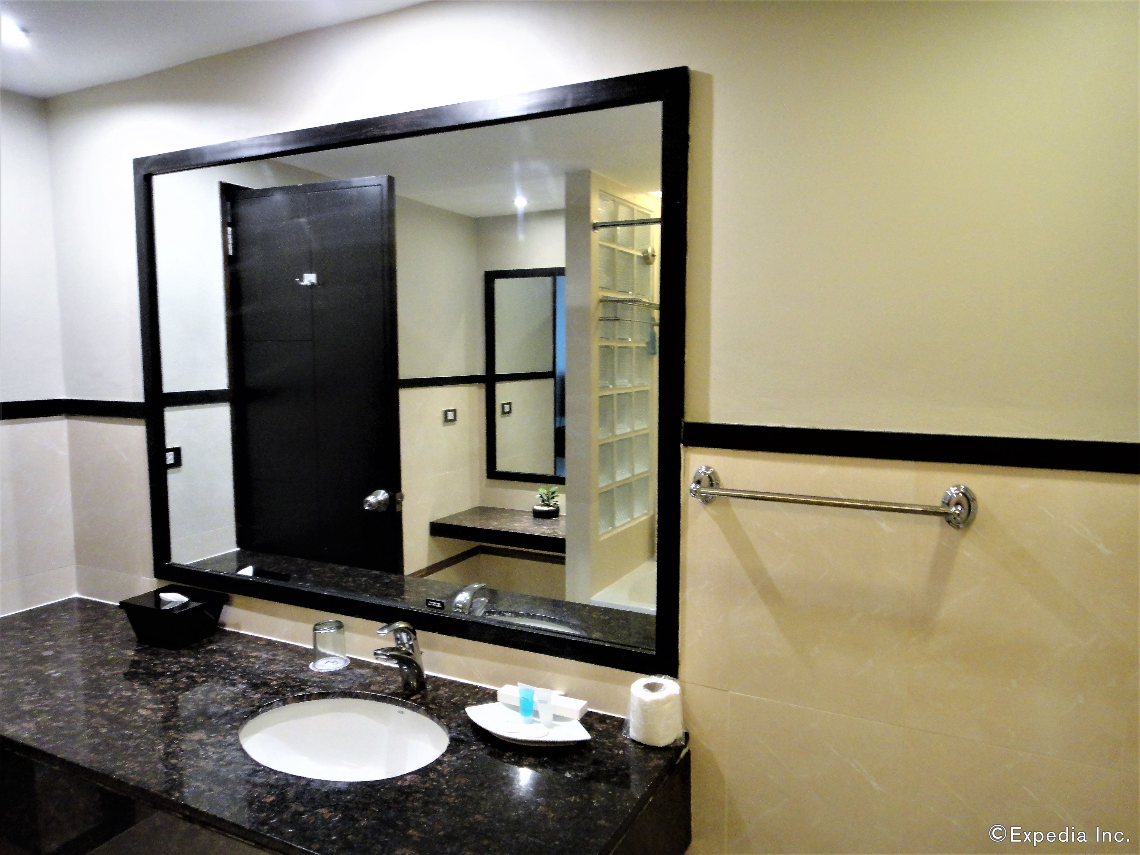 A bathroom with a large mirror, a sink, a towel rack, and a toilet paper dispenser.