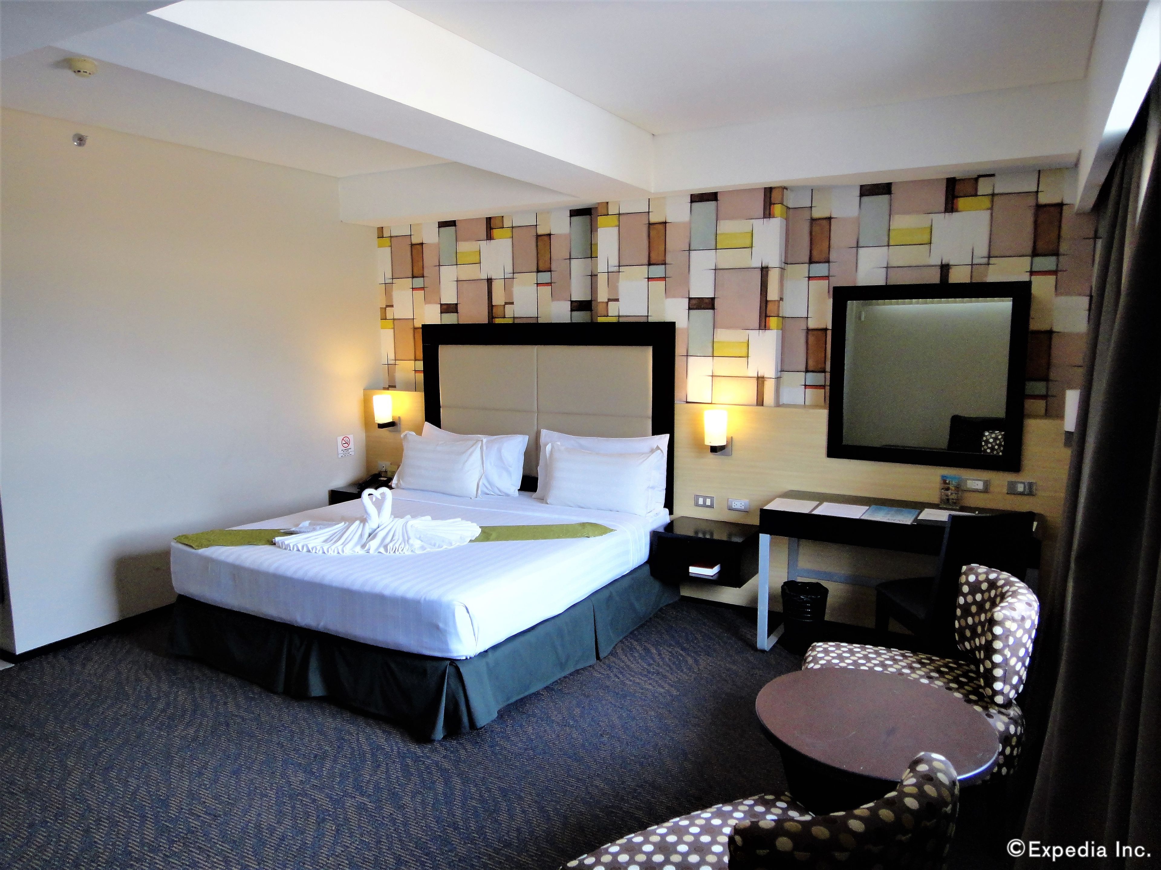A hotel room with a large bed, a desk, a chair, and a mirror.