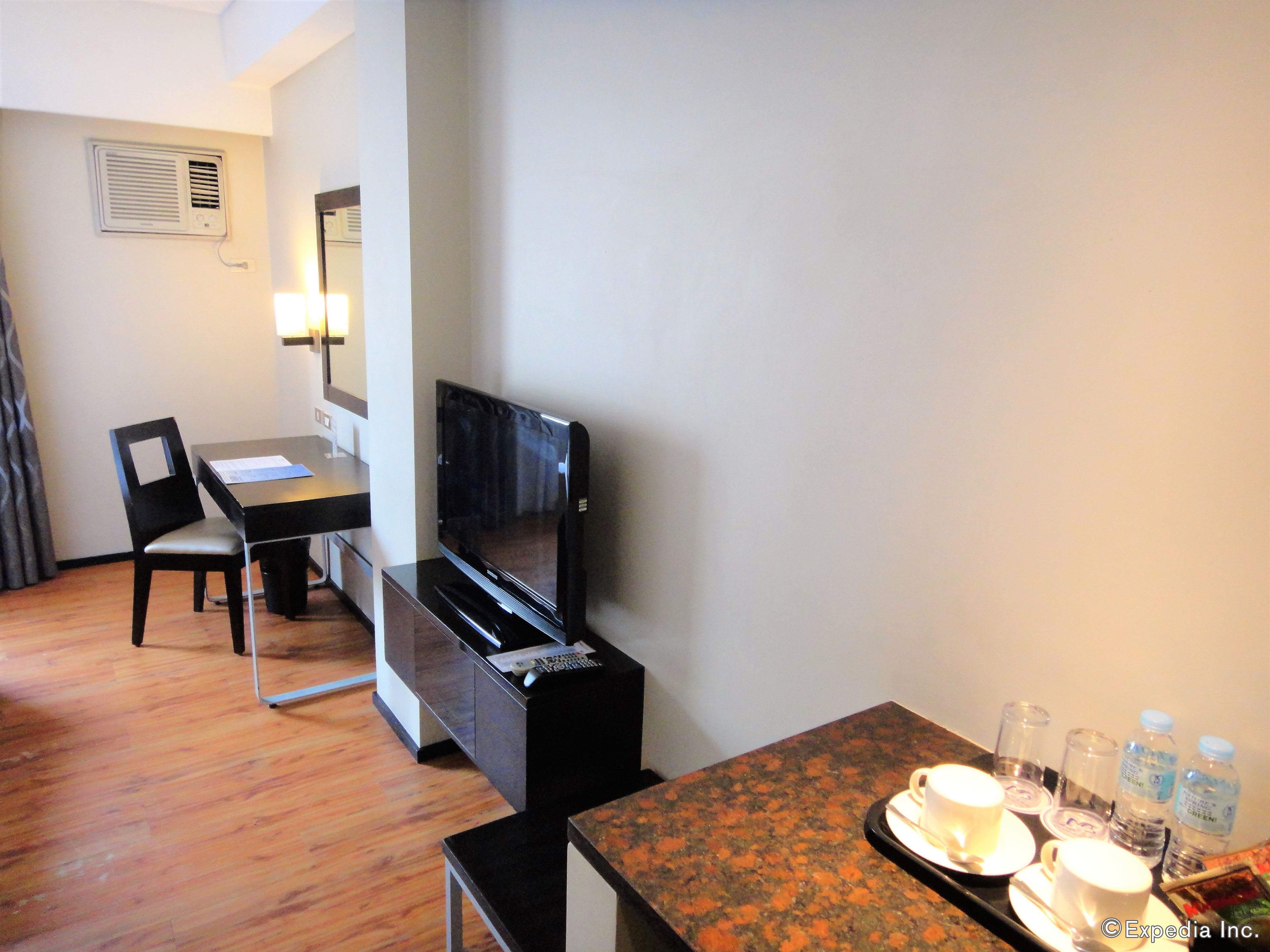 A hotel room with a desk, chair, TV, and a dining area with a table set for two.