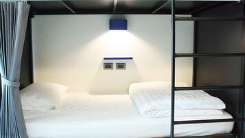 Un lit superposé avec une literie blanche et une tête de lit dotée d’un luminaire.