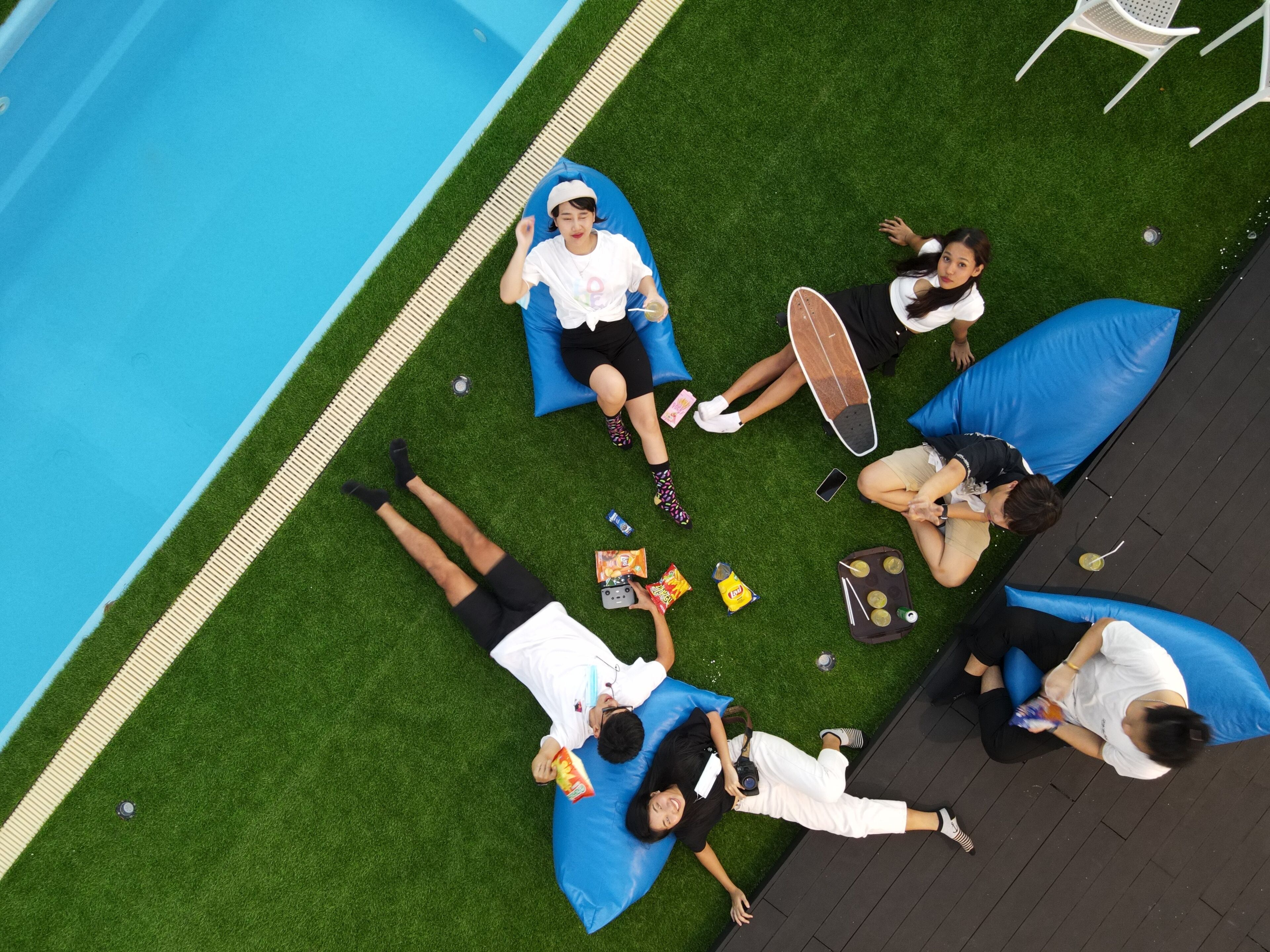 A group of people relaxing on blue bean bags by a poolside.