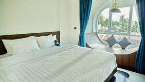Una cama con ropa blanca, cabecera de madera y ventana con vista a palmeras.